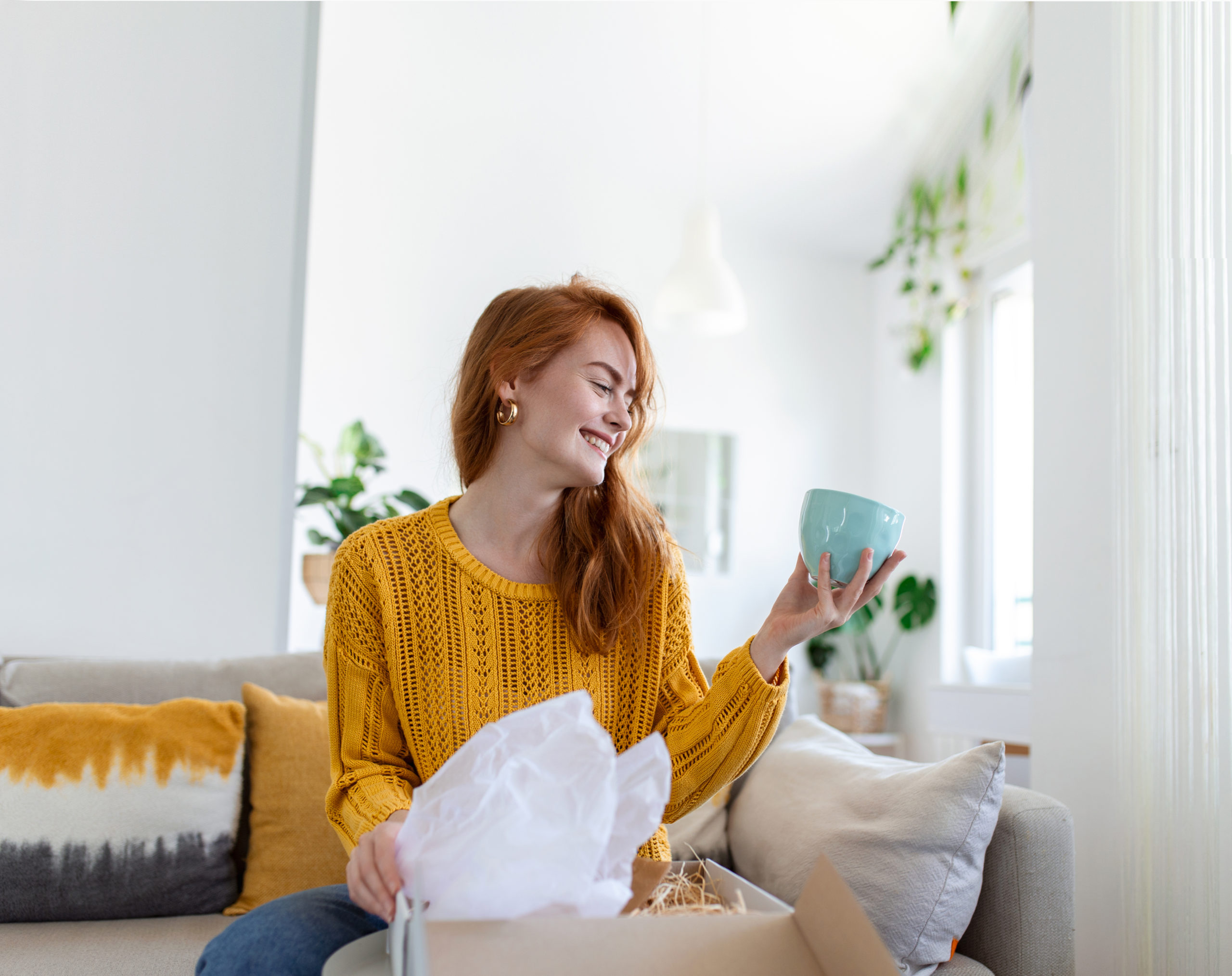 Female consumer unpack parcel receive retail purchase fast postal shipping delivery concept. Beautiful young woman is holding cardboard box sitting on sofa at home.