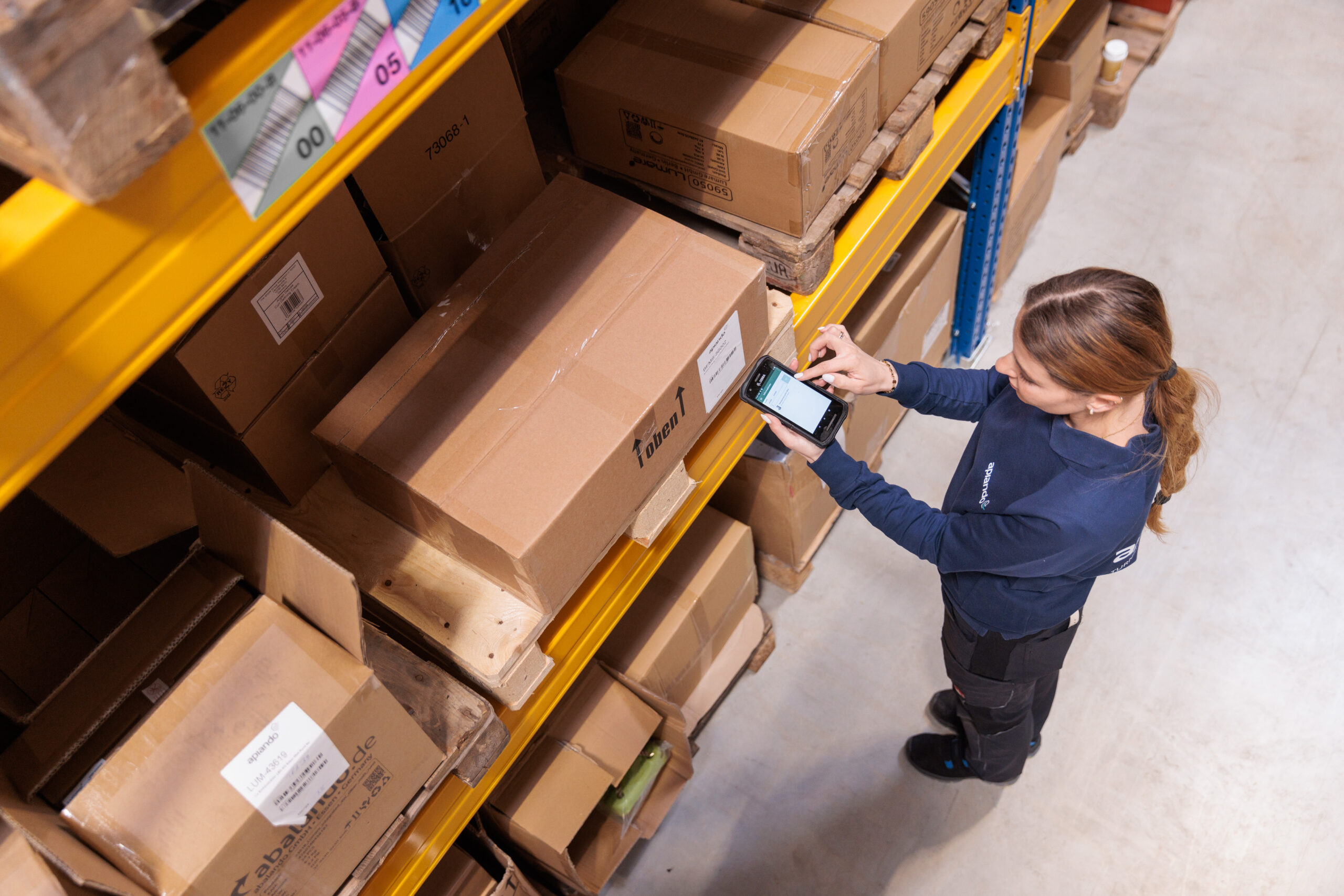 A young woman scans a parcel on a pallet on a warehouse shelf. 